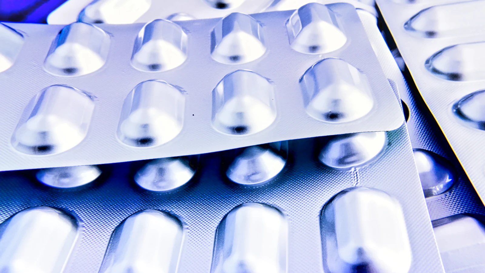 Varios blísteres de medicamentos superpuestos, sin etiquetas, con iluminación azulada