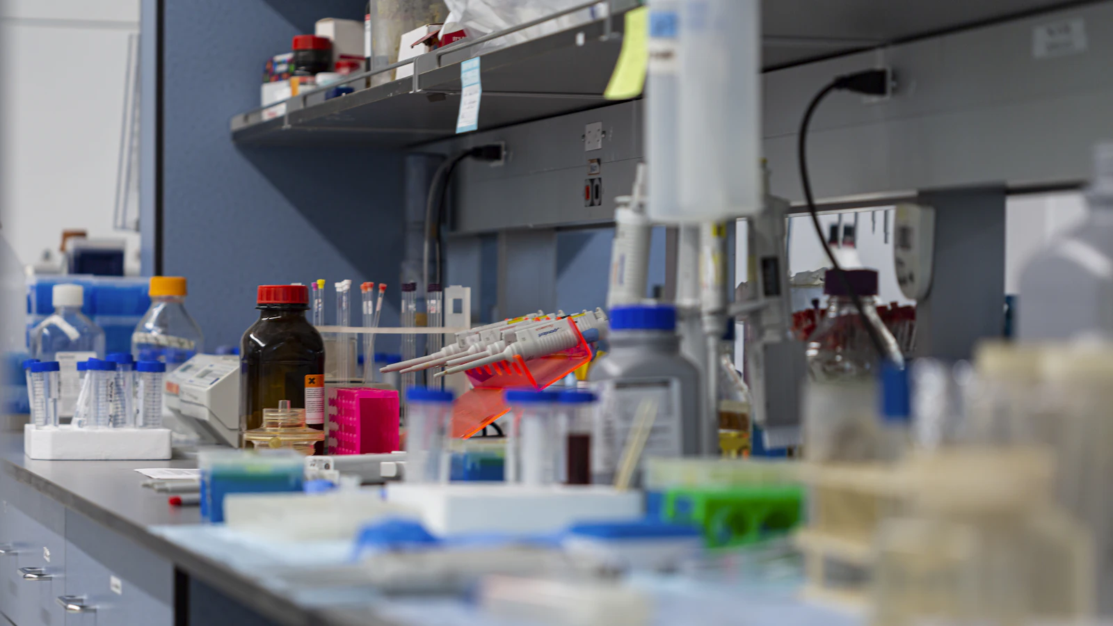 Mesa de un laboratorio de química con frascos de reactivos, gradillas de tubos y micropipetas